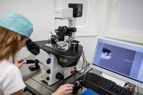 Expertka se dívá do mikroskopu. 