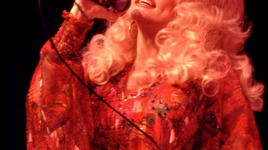 1977 – Hladce vyčesané, rozfoukané vlny doplněné hustými řasami a lesklými rty, epitom jižanského "tease-it-to-Jesus" glamouru. 1977 – Hladce vyčesané, rozfoukané vlny doplněné hustými řasami a lesklými rty, epitom jižanského "tease-it-to-Jesus" glamouru.